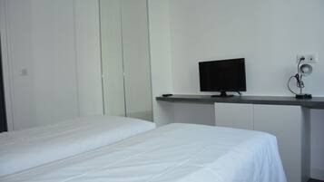 A hotel room with a bed, a desk with a computer monitor, and a mirror.