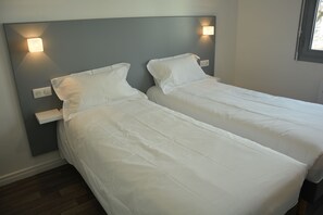A bedroom with two single beds, a nightstand, and wall-mounted lighting. - Le Matisse (Pau)