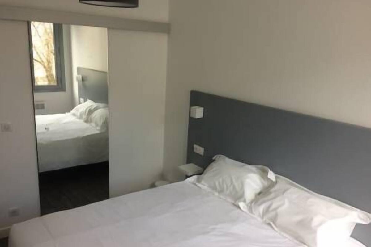 Una habitación de hotel con una cama, cabecera y ventana.