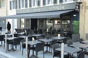 An outdoor cafe with tables and chairs, a menu board, and a person walking by. - Le Matisse (Pau)