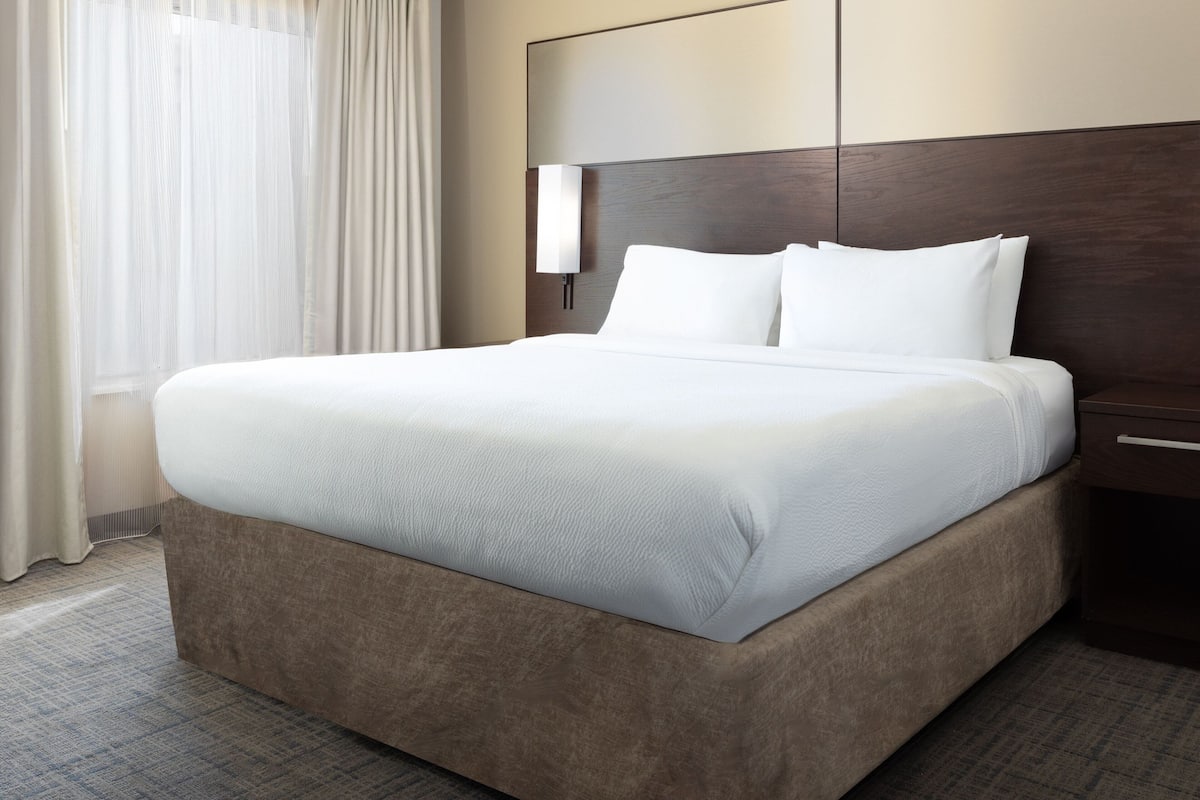 A large, neatly made bed with white linens in a hotel room.