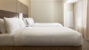 A modern hotel room with a large bed, a headboard, and a large window with curtains.