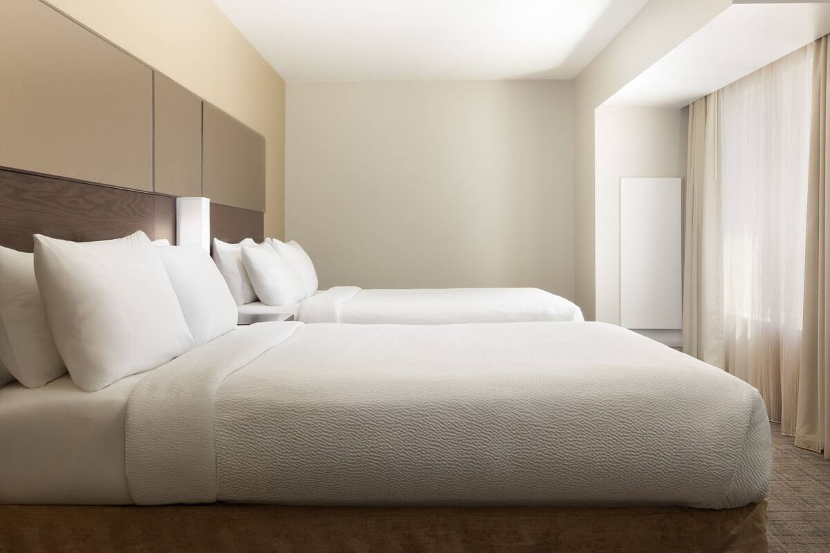 A modern hotel room with a large bed, a headboard, and a large window with curtains.