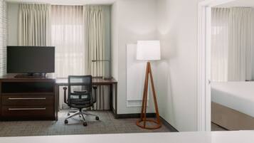 A hotel room with a bed, a desk with a computer, a chair, a TV, and a lamp.