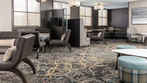 A hotel lobby with seating areas, a patterned carpet, and large windows.
