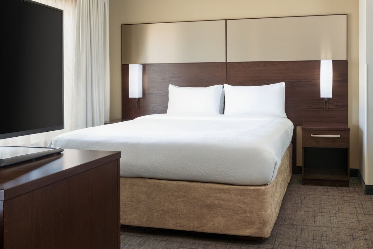 A hotel room with a large bed, a bedside table, a TV, and a nightstand.
