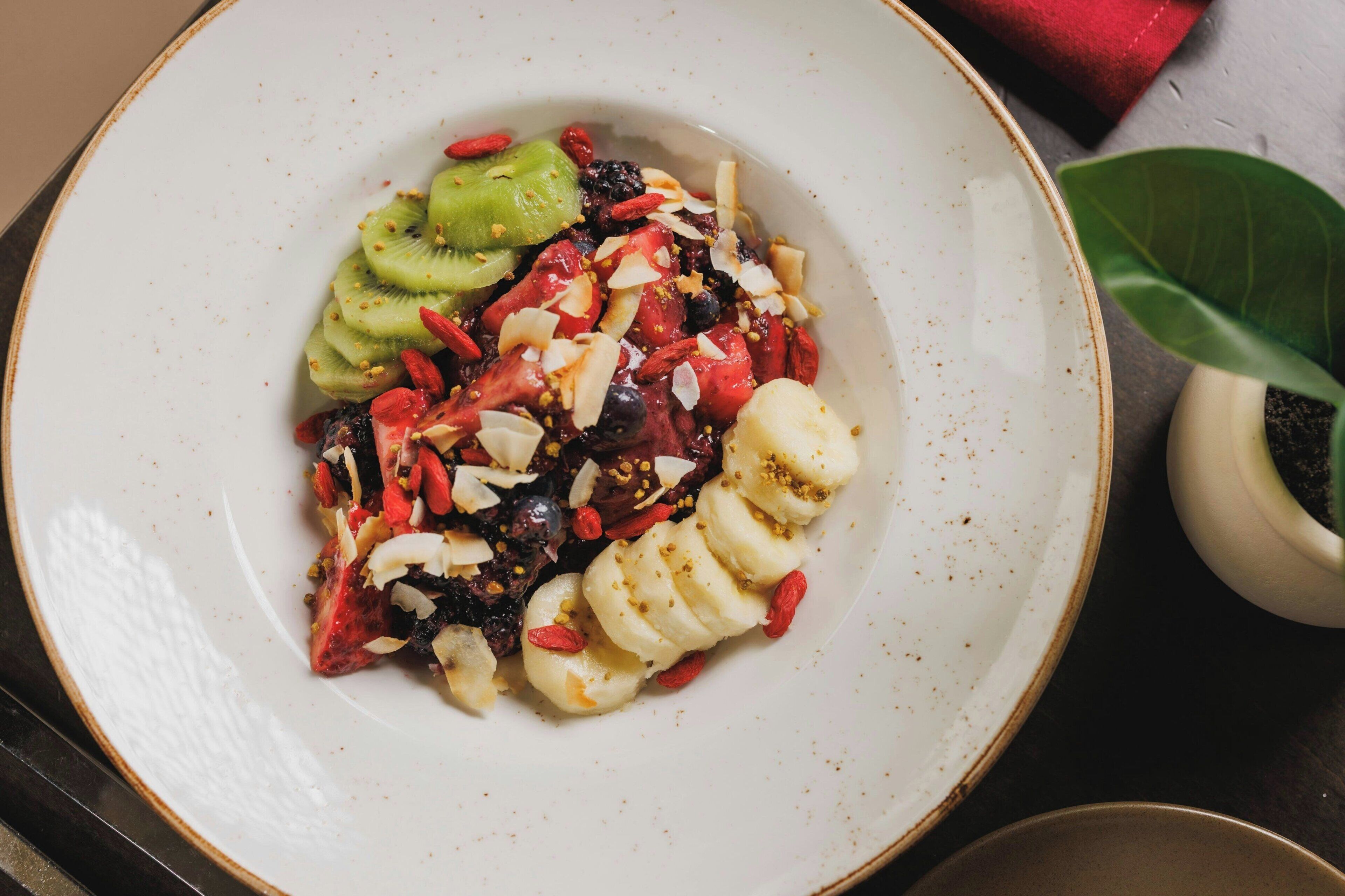 Ein weißer Teller mit Scheiben von Kiwi, Erdbeeren und Banane, belegt mit Samen und Nüssen.