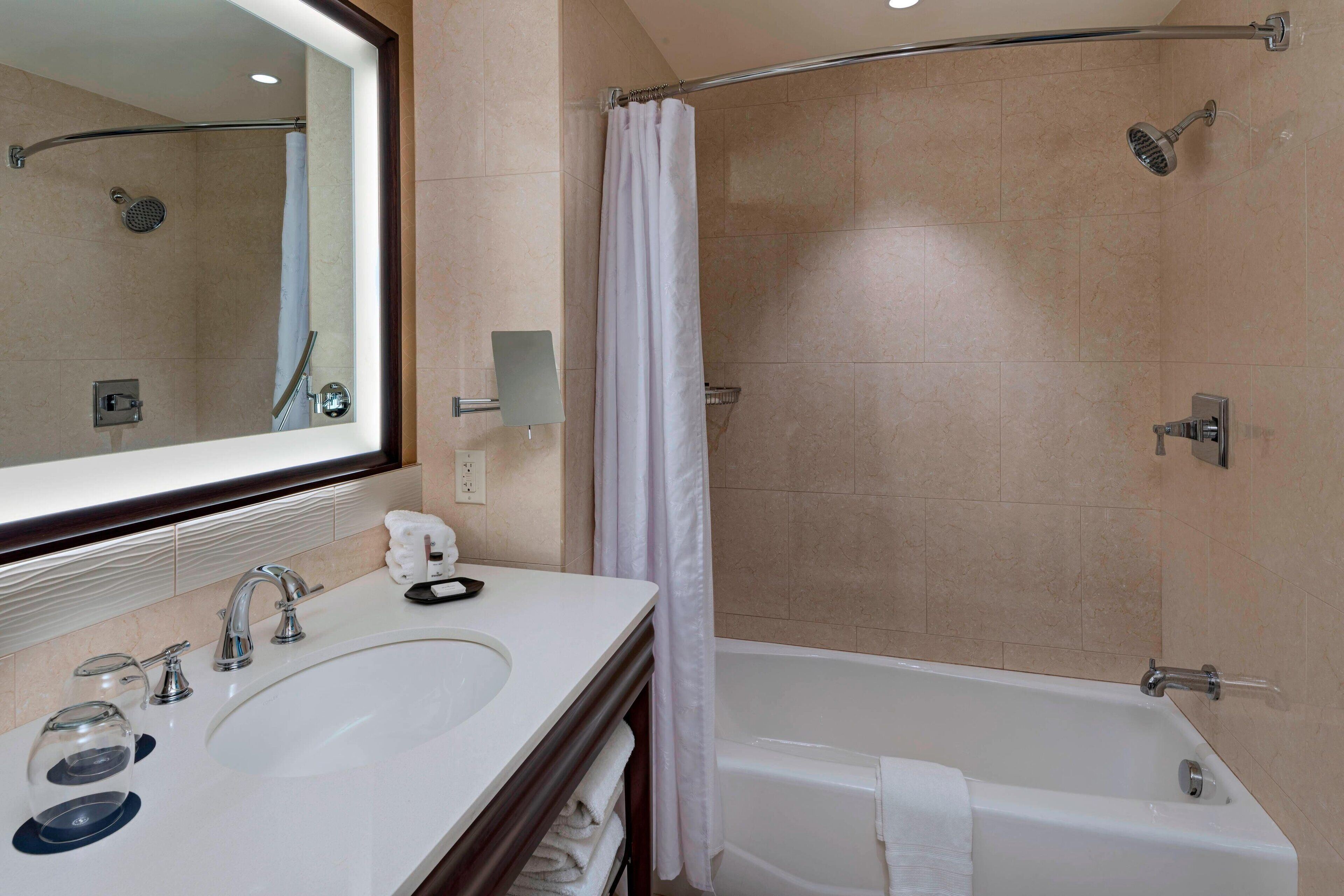 A modern bathroom with a large mirror, two sinks, a bathtub, and a shower.