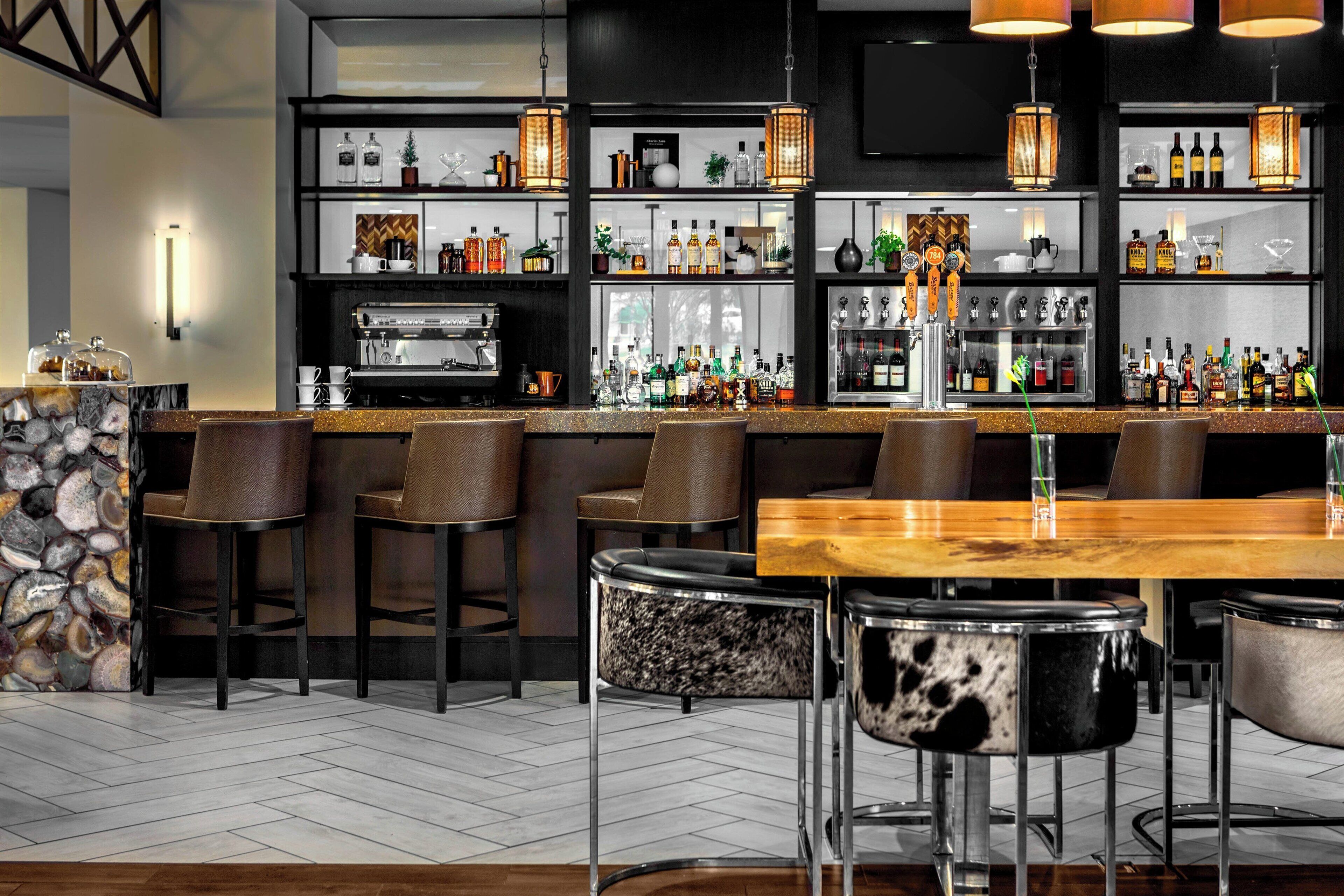 A bar area with a long counter, multiple stools, and a variety of bottles and glasses.