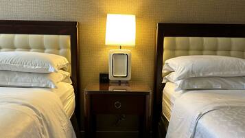 Habitación de hotel con dos camas, una mesita de noche con lámpara y un reloj digital.