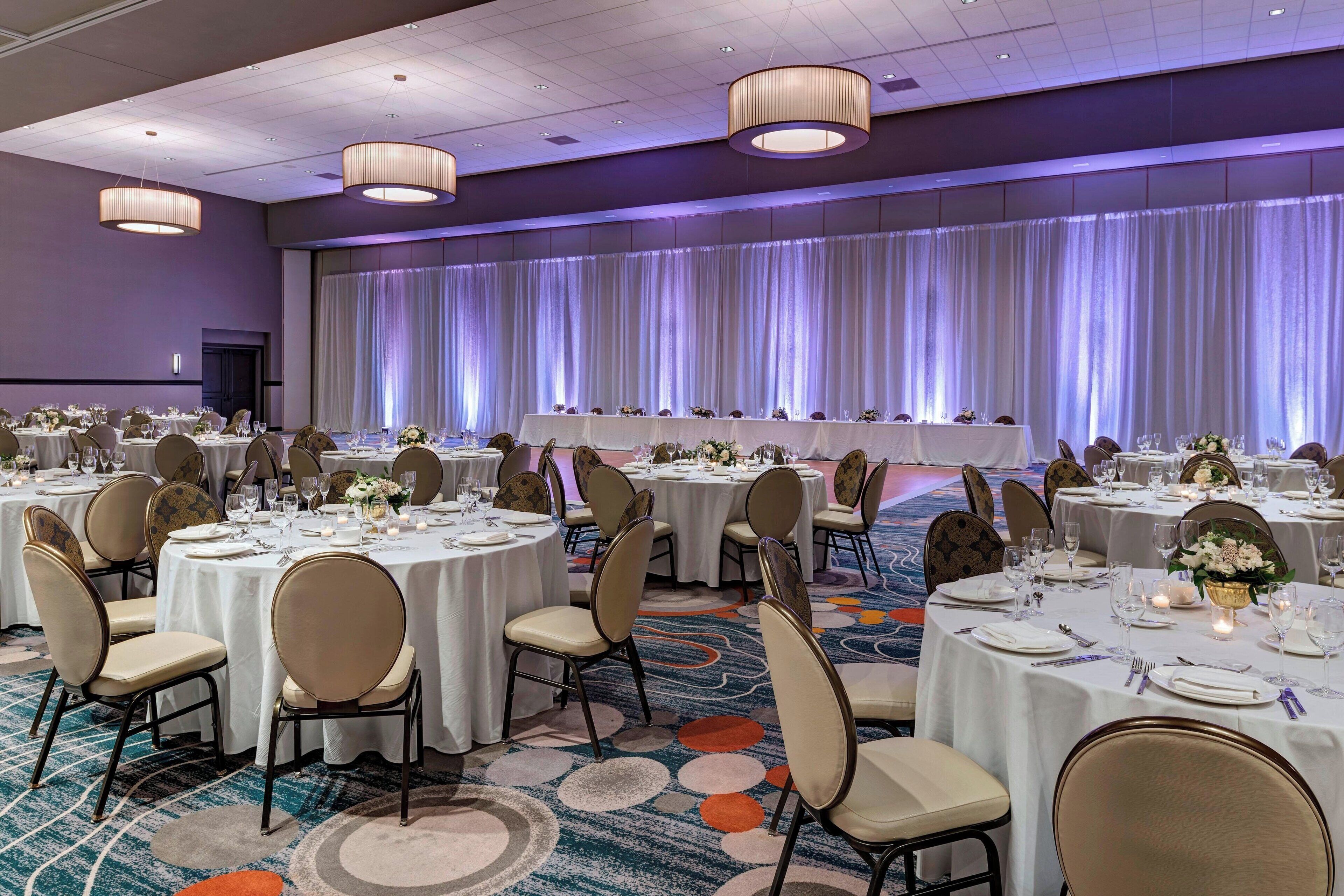 Une salle de banquet avec des tables rondes dressées pour le repas, agrémentées de nappes blanches et de chaises.