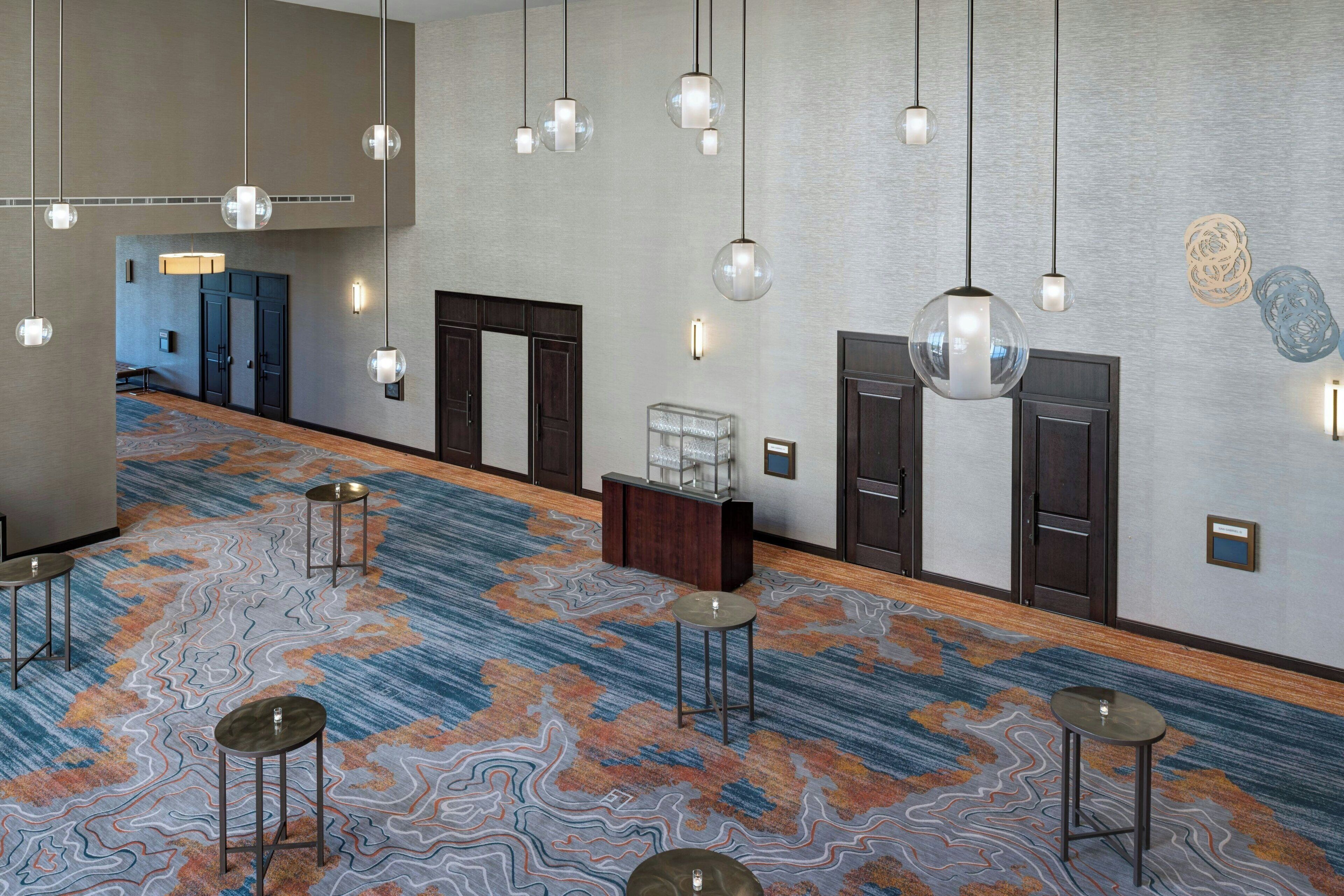 A hotel lobby with a patterned carpet, multiple seating areas, and pendant lighting.