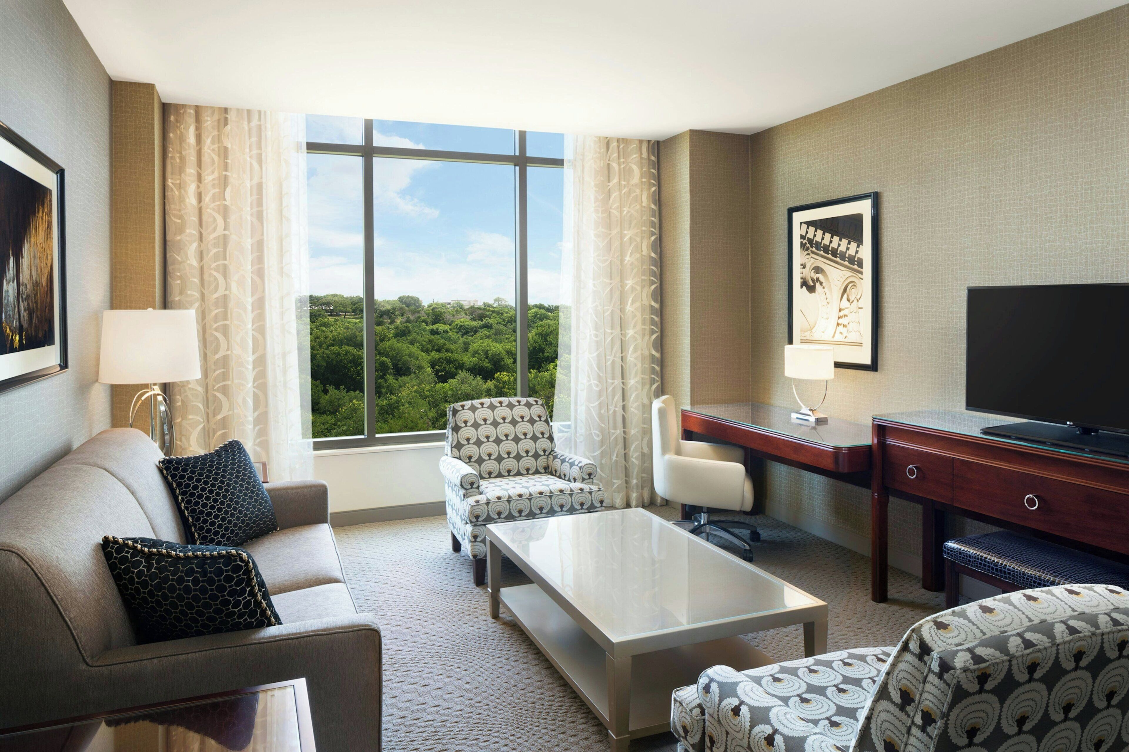 A hotel room with a sofa, armchair, desk, and television.