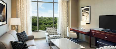 A hotel room with a sofa, armchair, desk, and television.