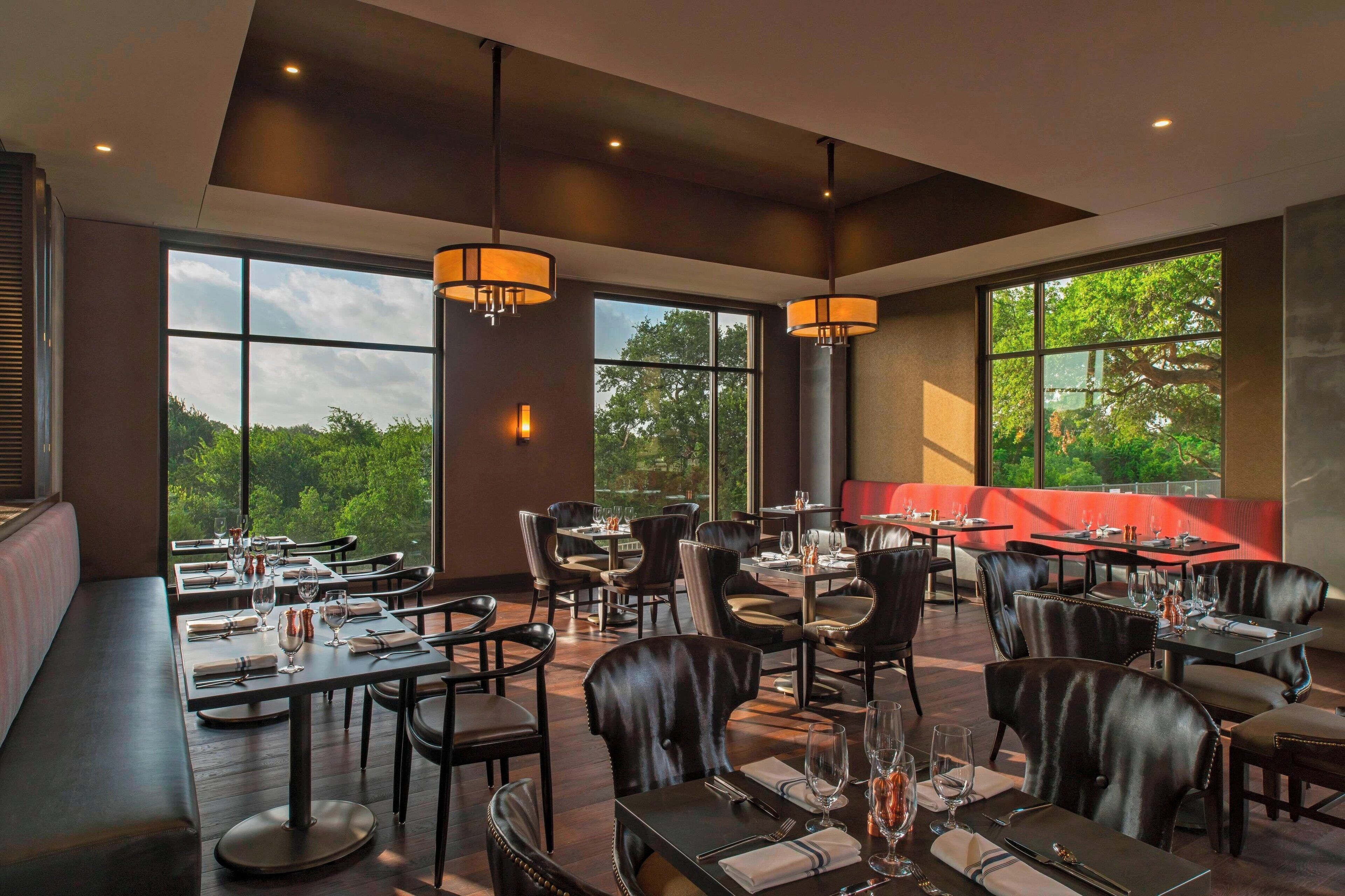 A restaurant with high ceilings, large windows, and leather seating. Tables are set with wine glasses and cutlery.
