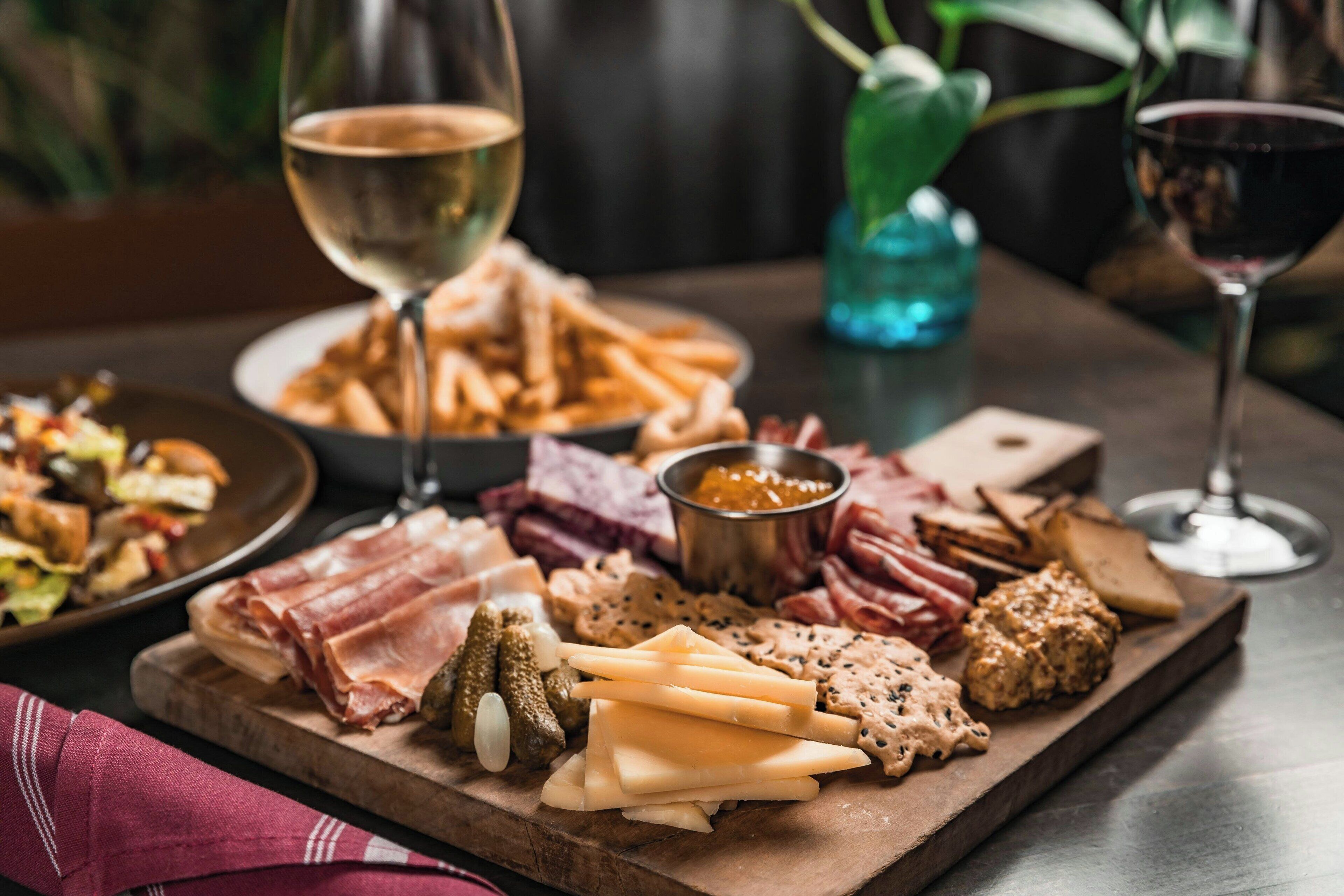 A charcuterie board with various meats, cheeses, and pickles, accompanied by glasses of wine.