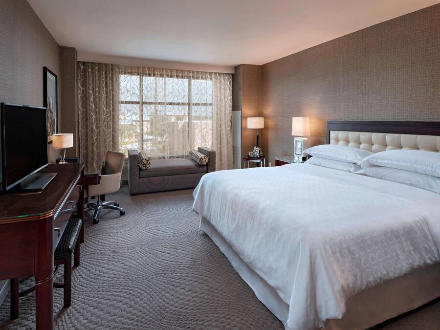Une chambre d’hôtel avec un grand lit, un bureau avec une télévision, une chaise et une fenêtre avec des rideaux.