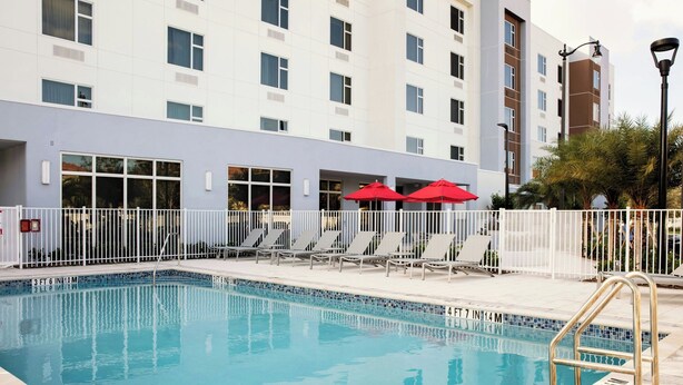 A swimming pool with a white fence, red umbrellas, and lounge chairs.