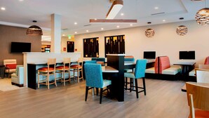 A modern hotel lobby with a bar area, seating arrangements, and a flat-screen TV mounted on the wall.