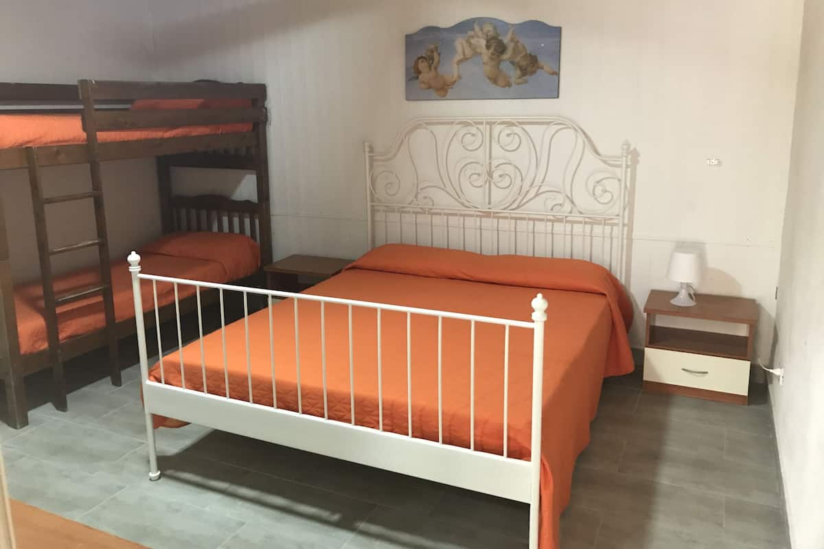 Ein Zimmer mit einem Etagenbett, einem Einzelbett, einem Nachttisch, einer Lampe und einem Bild an der Wand.