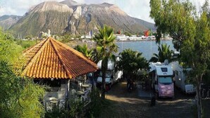 Ein Campingplatz mit Wohnmobilen, einem kleinen Gebäude mit Ziegeldach und einem Berg im Hintergrund.