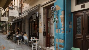 Un café en plein air avec des tables et des chaises, une porte bleue et une enseigne indiquant « MORFEAS ».