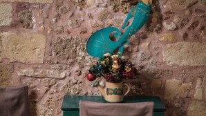 Une pièce rustique avec un mur en pierre, une chaise en bois, une petite table ornée d’un vase de fleurs et une statuette décorative représentant une sirène.