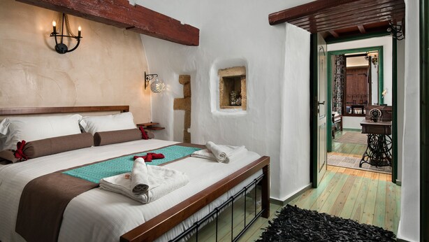 Un lit bien fait, avec une tête de lit en bois, un luminaire fixé au mur et une petite fenêtre donnant sur la pièce.