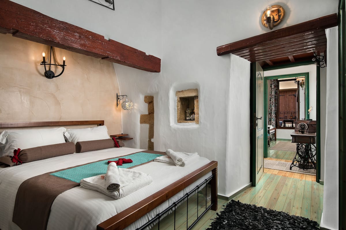 A neatly made bed with a wooden headboard, a wall-mounted light fixture, and a small window with a view of the room.