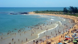 Una playa concurrida con gente y sombrillas, cielo despejado y mar tranquilo.