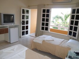 Quarto de hotel com cama, televisão, mini-frigorífico e varanda com vista para o verde.