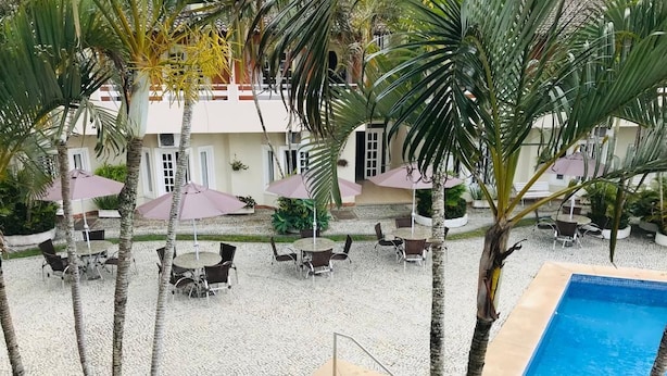 Zona de piscina con palmeras, mobiliario exterior y un edificio al fondo.
