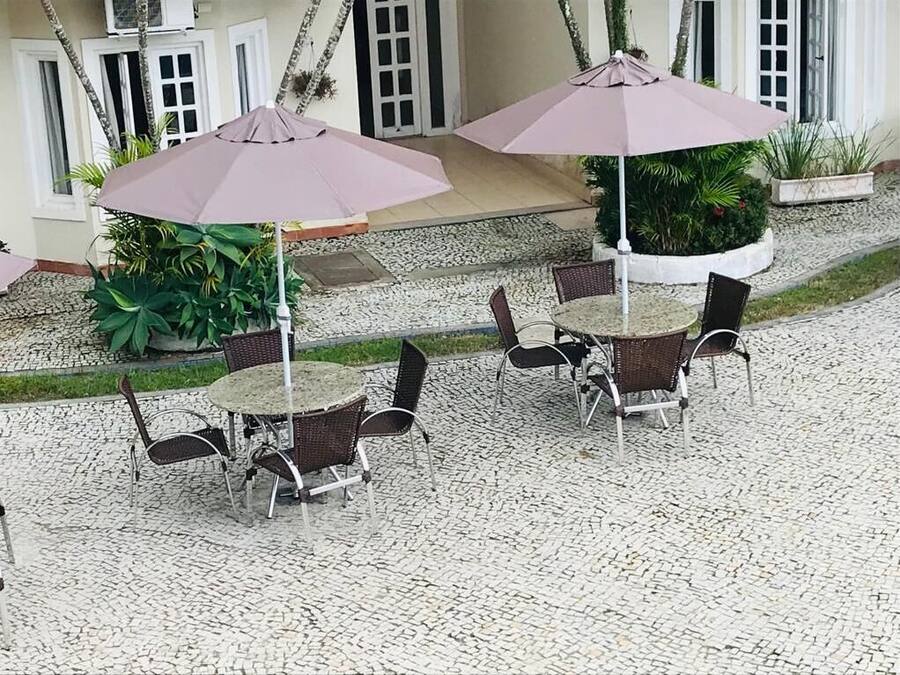 Un espacio al aire libre con mesas y sillas redondas, dos sombrillas y plantas en macetas.
