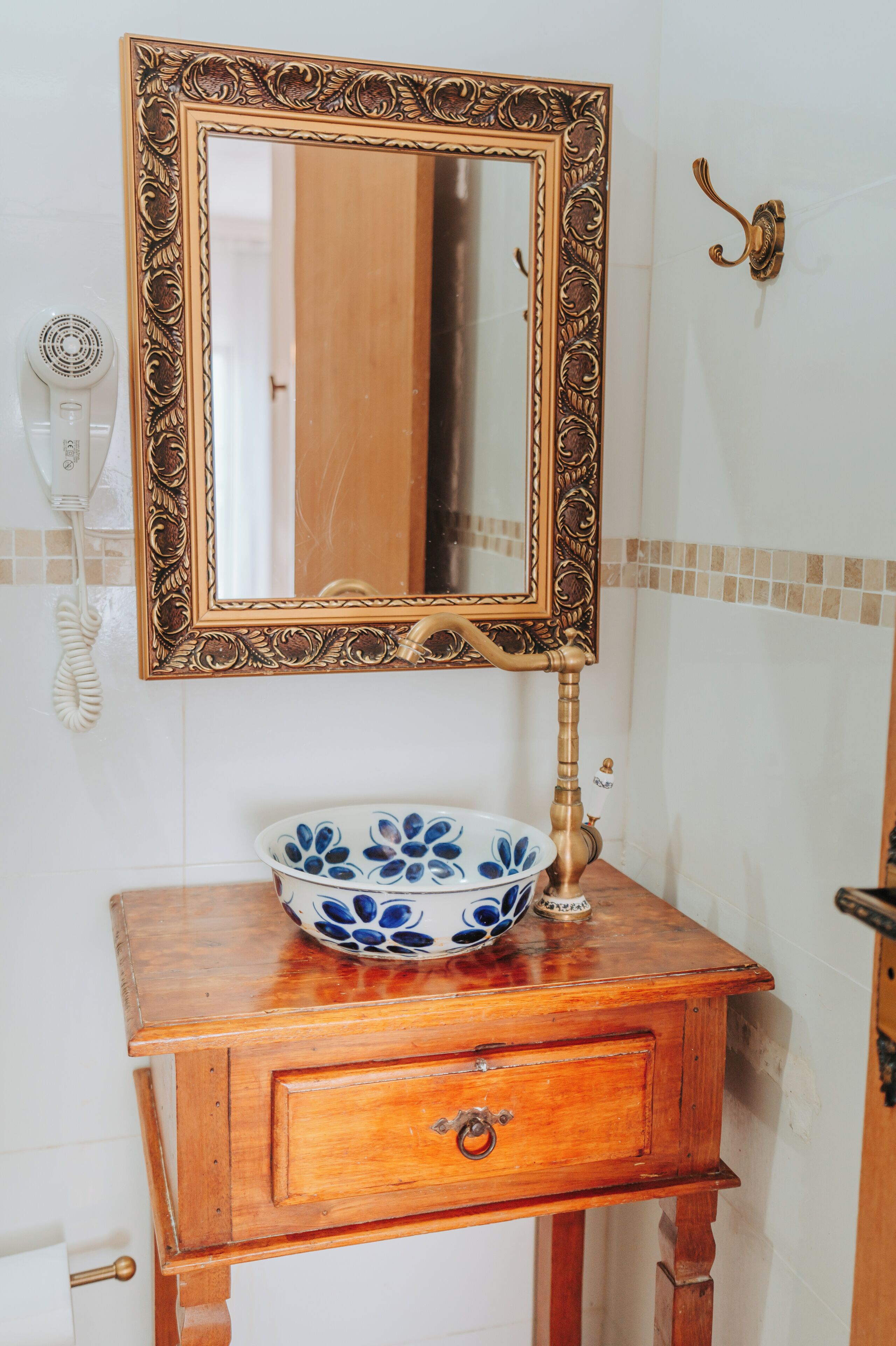 Un baño con tocador de madera, un espejo con marco ornamentado y un cuenco con motivos florales azules en la encimera.