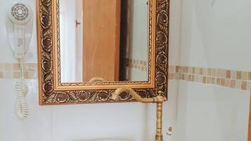 Un baño con tocador de madera, un espejo con marco ornamentado y un cuenco con motivos florales azules en la encimera.