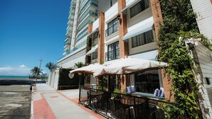 Un hôtel doté d’une terrasse, offrant une vue sur la plage et dont l’arrière-plan est dominé par un grand immeuble.