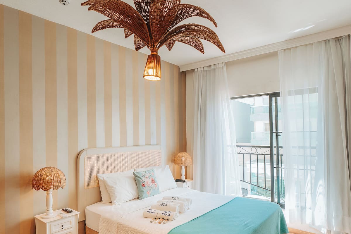 A hotel room with a bed, bedside tables, a hanging light fixture, and a view of the outside.
