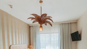 Une chambre à coucher comprenant un lit, des tables de chevet, un bureau, une chaise, un téléviseur et une fenêtre avec des rideaux.