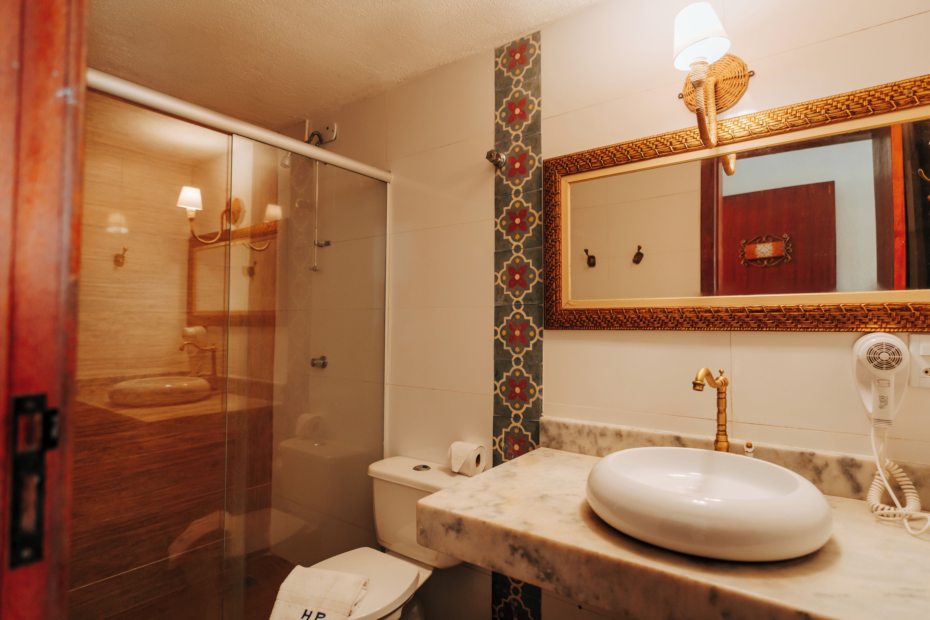 A bathroom with a glass-enclosed shower, a marble sink, a large mirror, and a hairdryer on the counter.