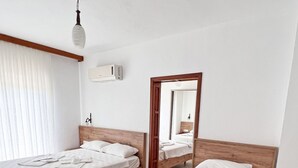 Una habitación de hotel con dos camas de madera, sábanas blancas, un ventilador de techo, un equipo de aire acondicionado y un espejo en la pared.