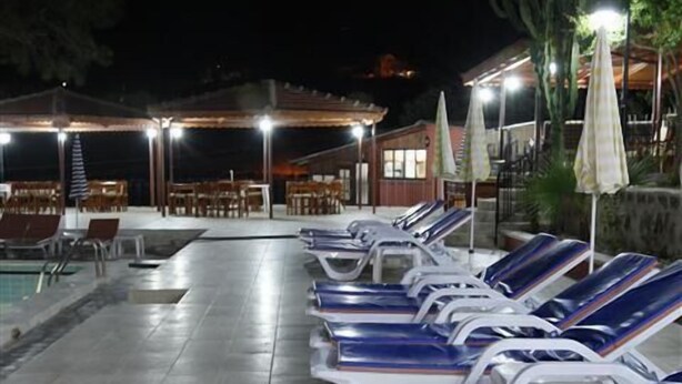 Zona junto a la piscina con sillones de descanso y sombrillas, una piscina y un edificio al fondo.