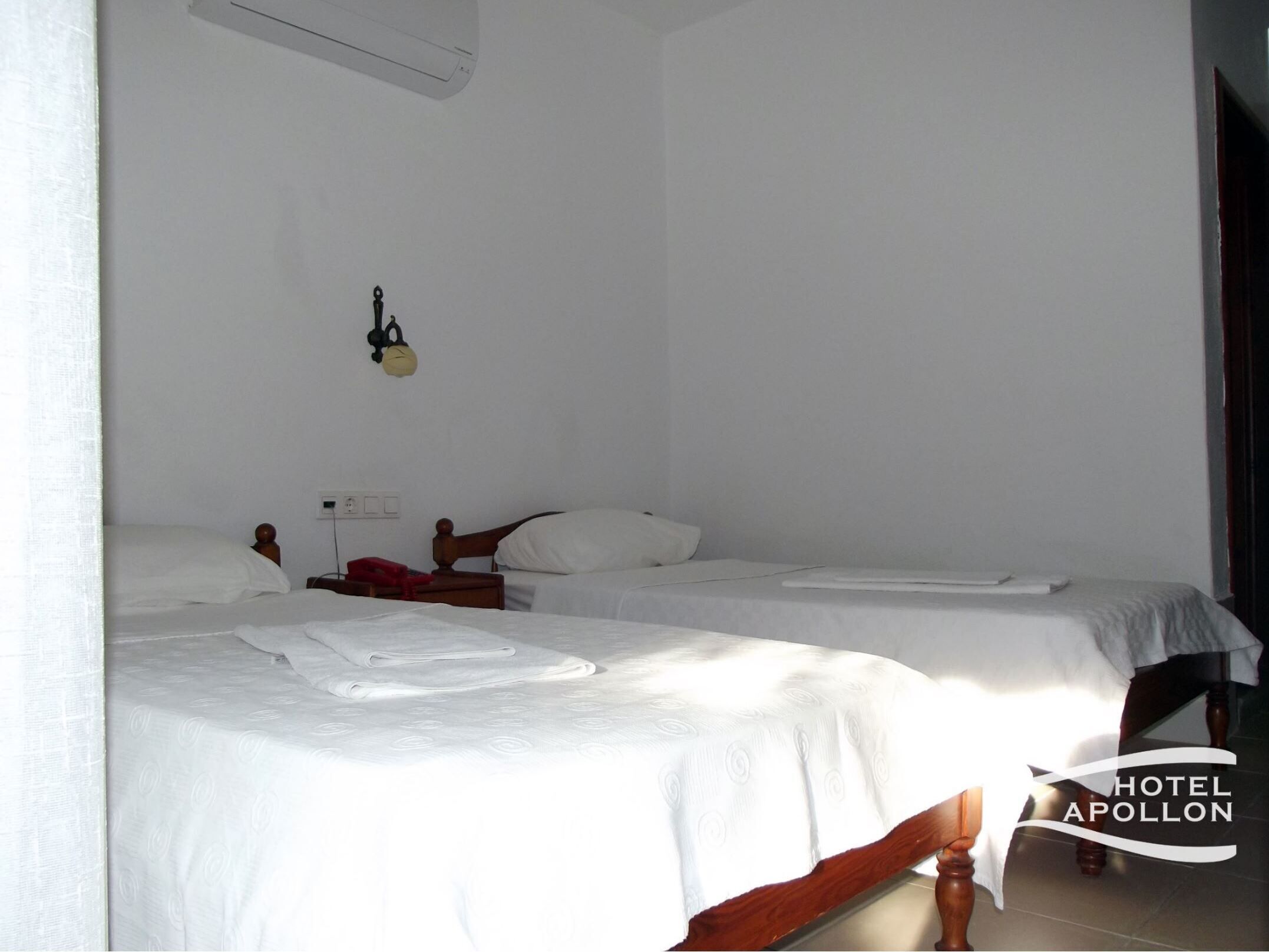 A hotel room with two single beds, a bedside table with a lamp, and a wall-mounted clock.