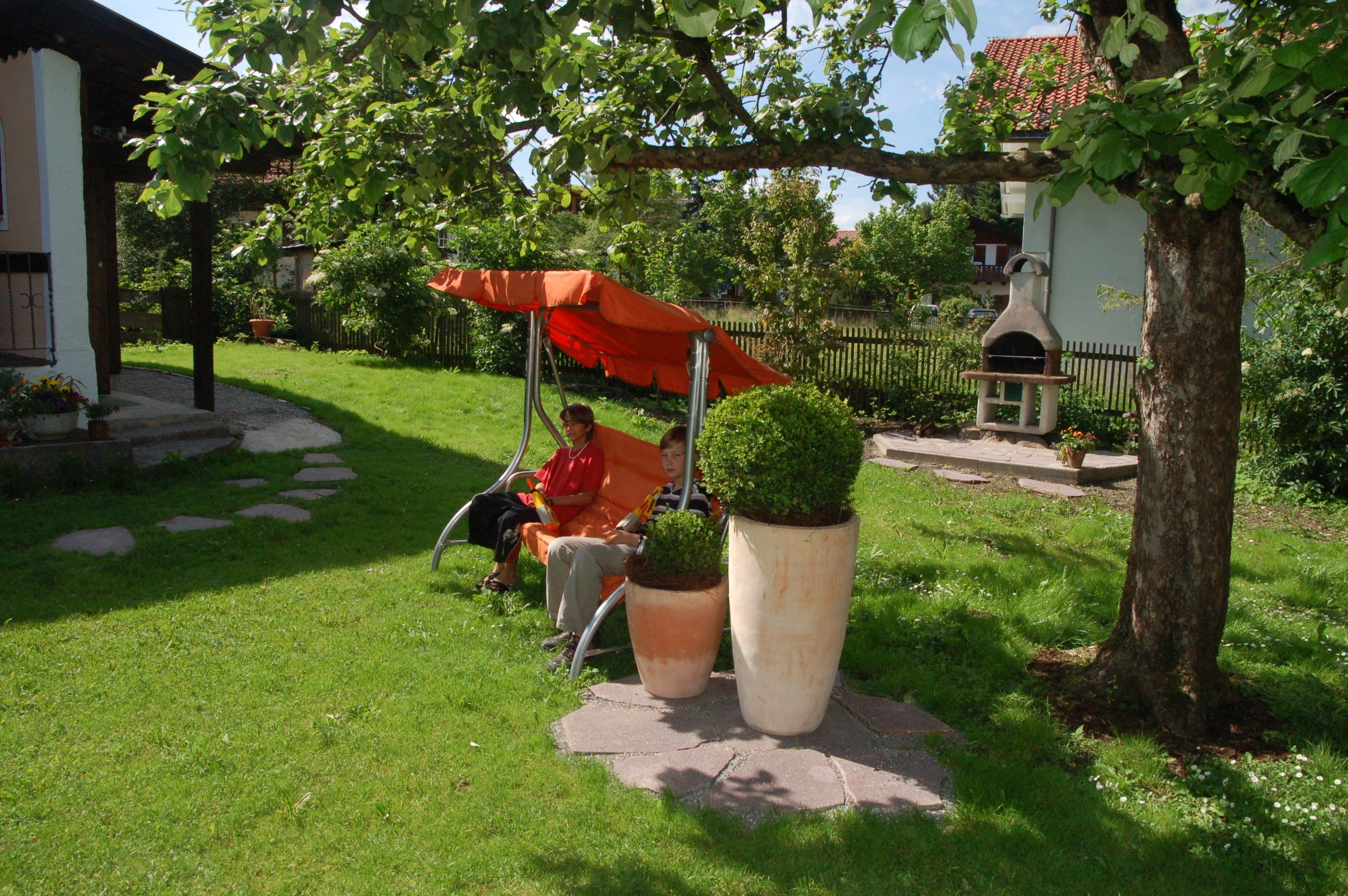Un'area giardino con altalene, grandi piante in vaso e un vialetto in pietra.