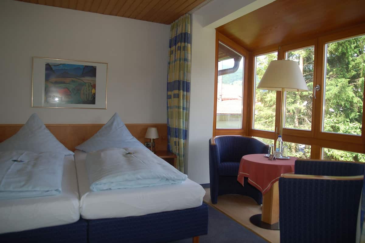 Ein Hotelzimmer mit zwei Betten, einem Tisch mit Lampe, einem Sessel und einem Bild an der Wand.