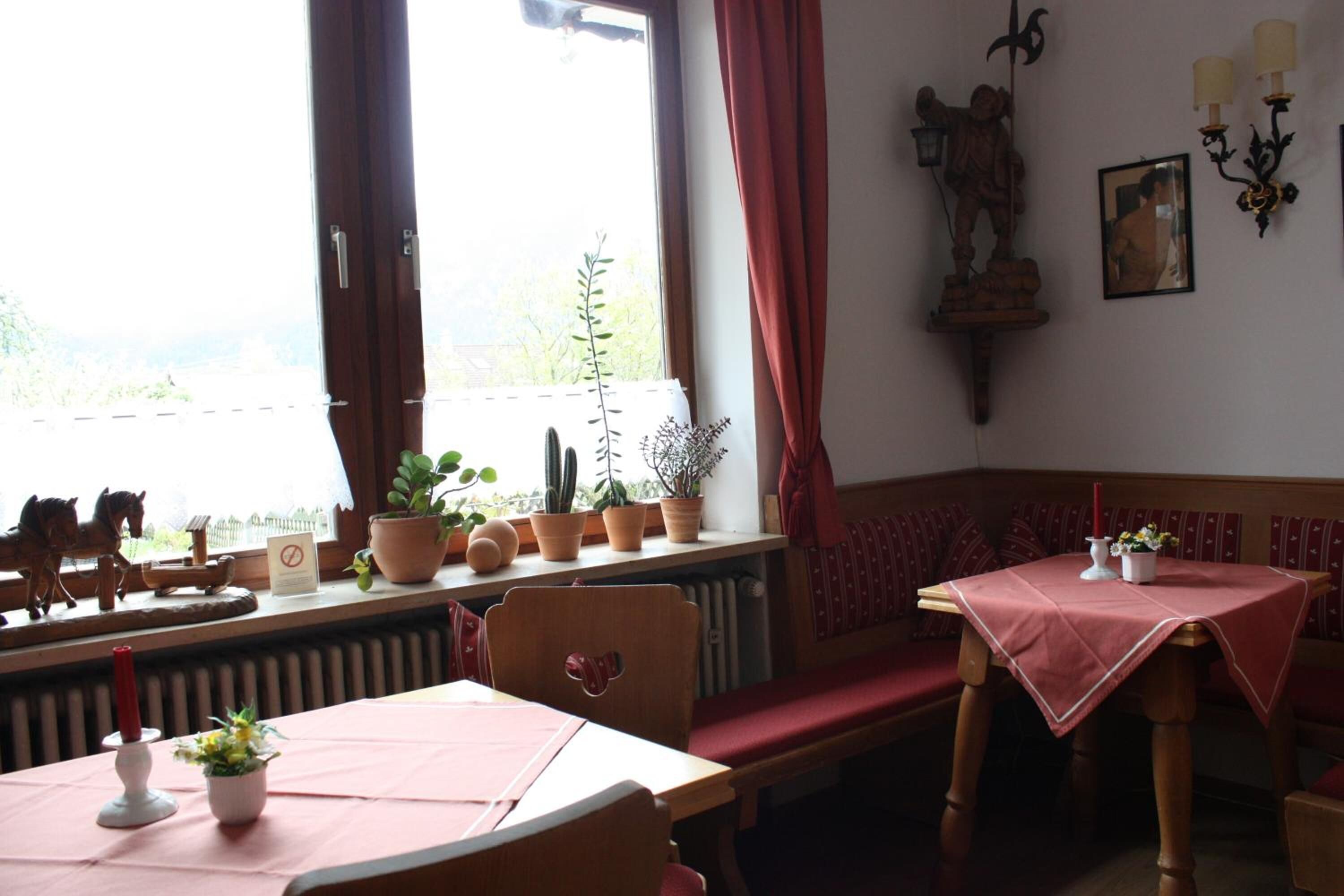 Un coin repas accueillant avec une table dressée pour deux personnes, un banc et une fenêtre agrémentée de plantes en pot.