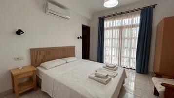 Un dormitorio con cama, mesita de noche, aire acondicionado, ventana con cortinas y una lámpara colgante.
