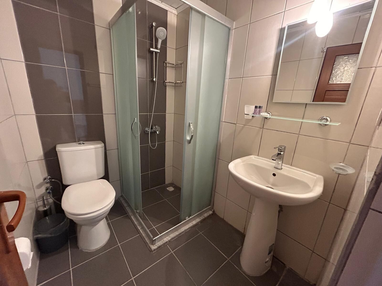 Un baño con inodoro, ducha con mampara de vidrio y lavamanos pedestal.