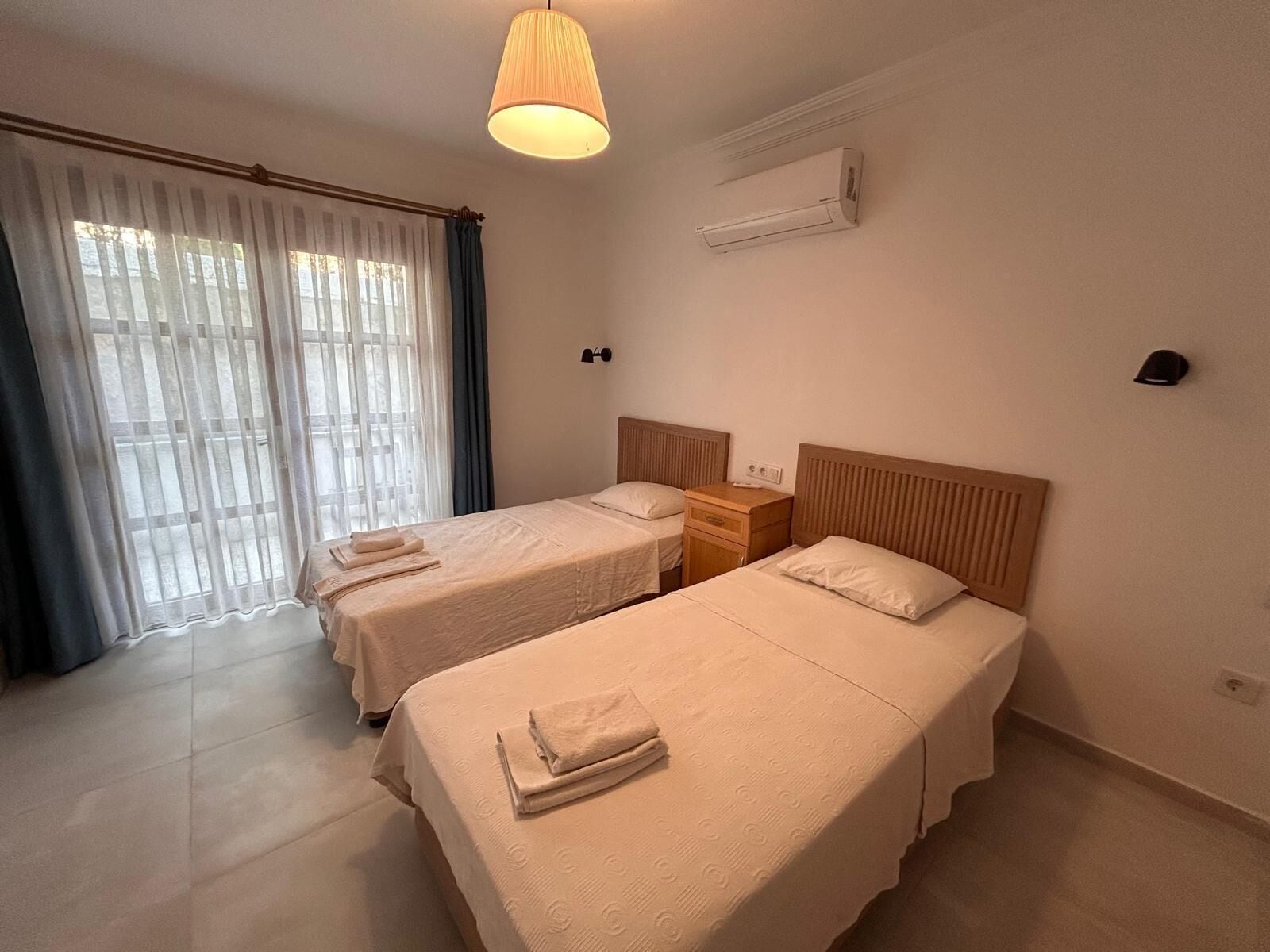 Habitación de hotel con dos camas, una mesita de noche, una lámpara, equipo de aire acondicionado y una ventana con cortinas.