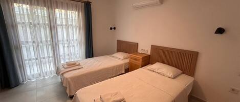 Habitación de hotel con dos camas, una mesita de noche, una lámpara, equipo de aire acondicionado y una ventana con cortinas.