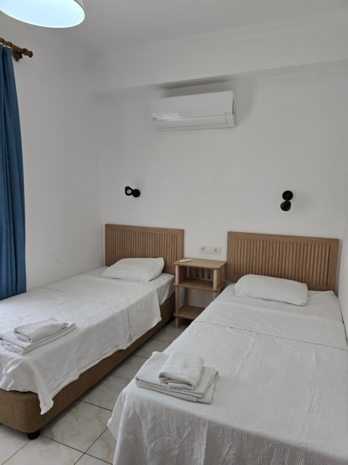 A room with two beds, a small table, and a wall-mounted air conditioner.